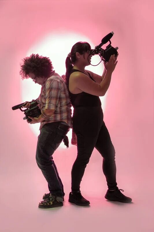 Shine Louise Houston and Ava LaPrima on a pink background holding video cameras